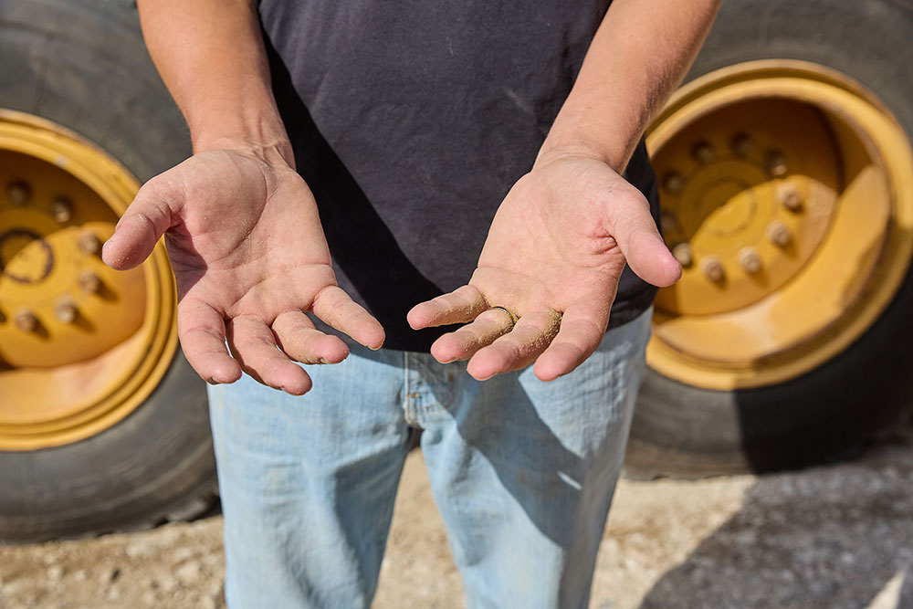 Close-up of Nick Castillion’s open hands, slightly dirty, held out in front of a large construction vehicle tire."